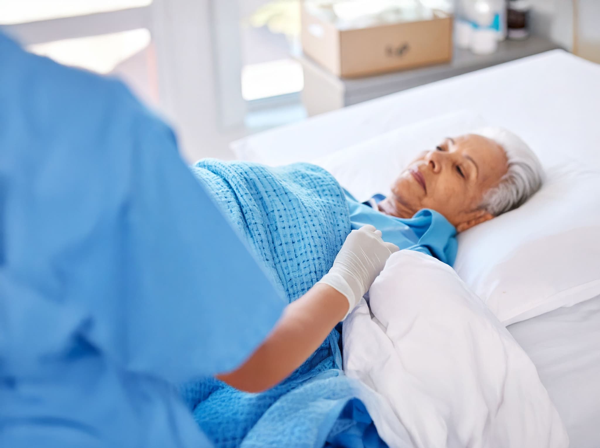 Pflegekraft deckt eine Seniorin im Krankenhausbett zu