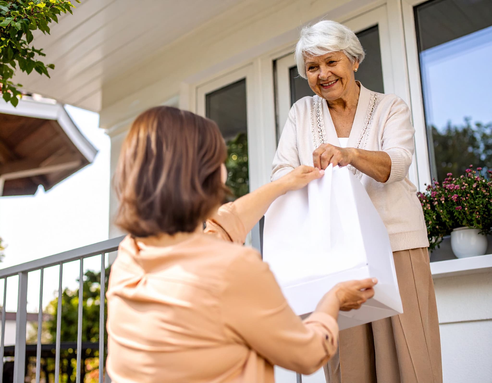 Seniorin nimmt eine Tüte mit Essen auf der Veranda eines Hauses entgegen