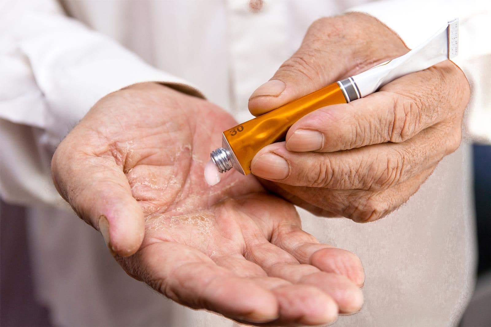 Senior drückt eine kleine Menge Creme aus einer goldfarbenen Tube auf die Handfläche