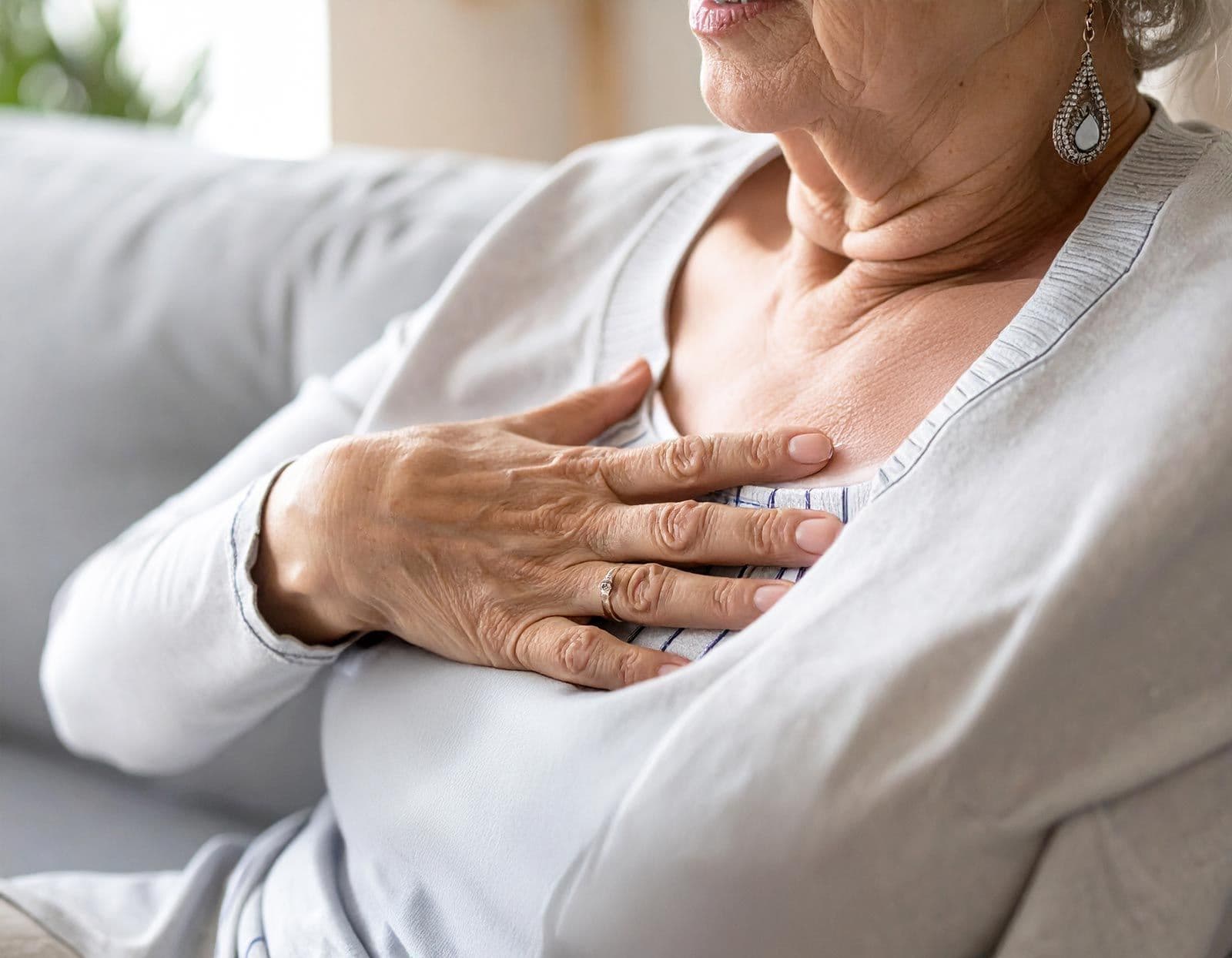 Seniorin sitzt auf Sofa und hält schmerzhaft ihre Brust mit der Hand