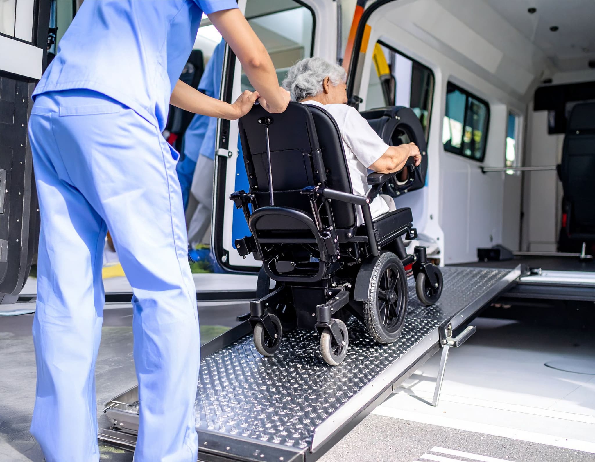 Pflegekraft hilft Seniorin im Rollstuhl über Rampe in einen Krankentransport