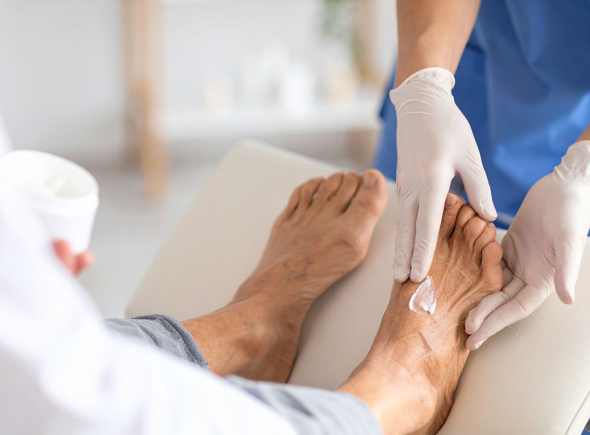 Pflegekraft mit Handschuhen trägt Creme auf die Füße einer älteren Frau auf