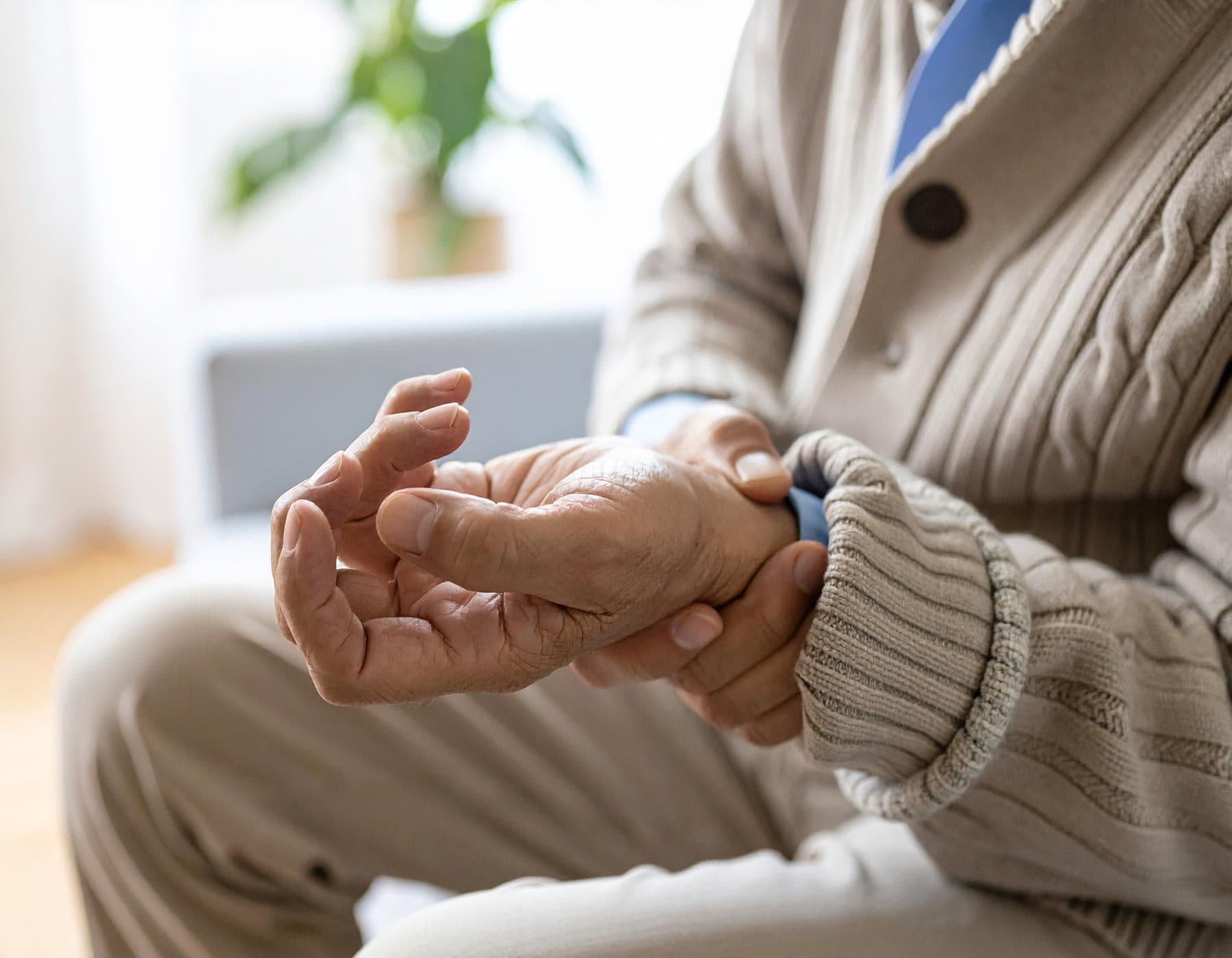 Nahaufnahme der Hände eines älteren Mannes mit Parkinson, eine Hand ist verkrampft und wird von der anderen gehalten