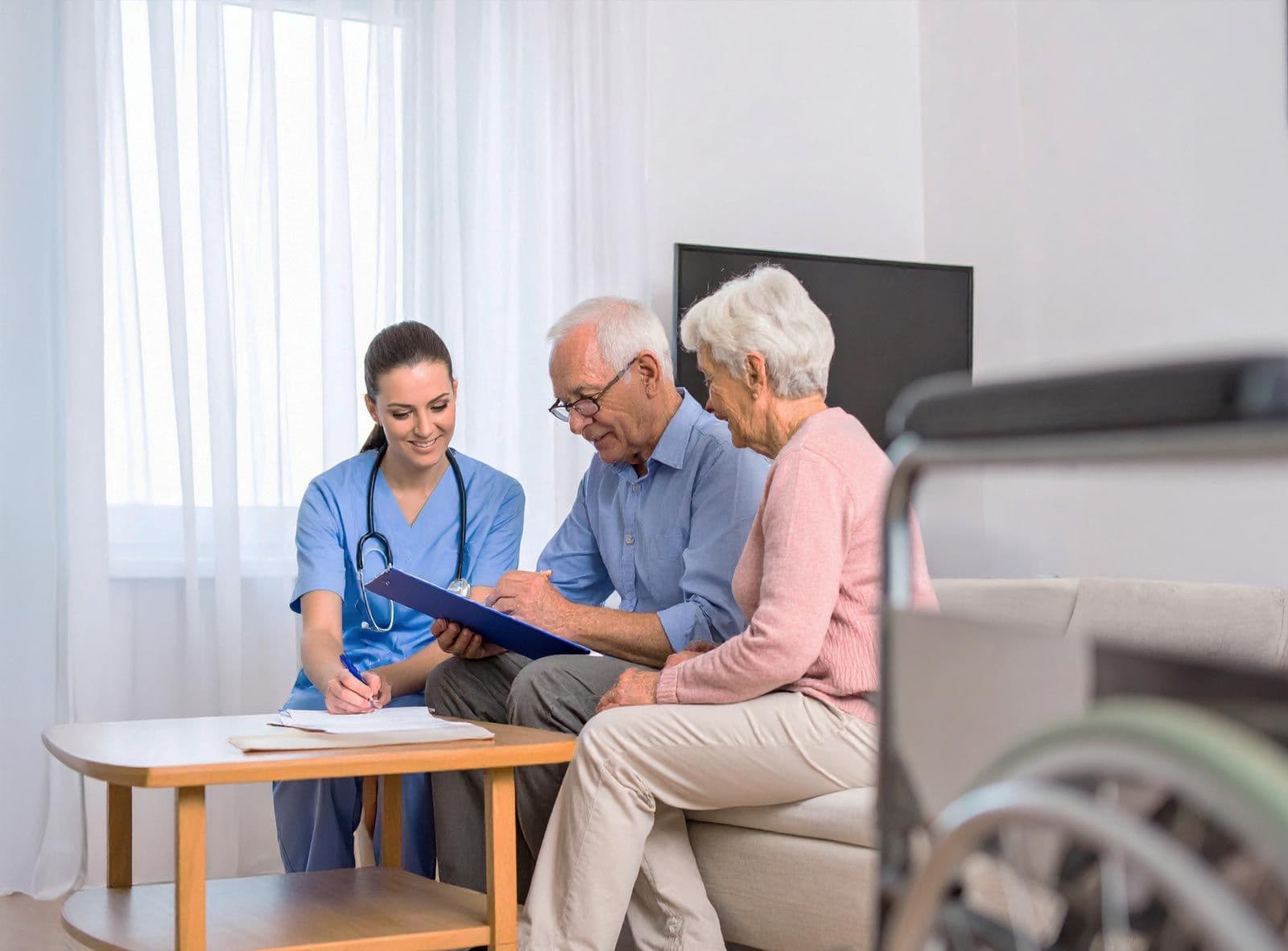 Pflegekraft berät älteres Paar im Wohnzimmer, sie sitzen am Tisch mit Unterlagen
