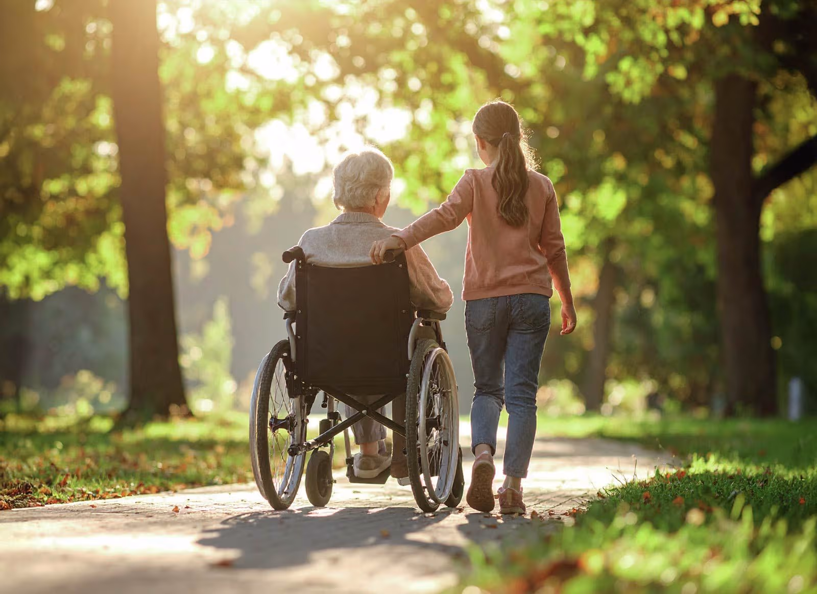 Mädchen schiebt ältere Frau im Rollstuhl auf einem Weg im Park