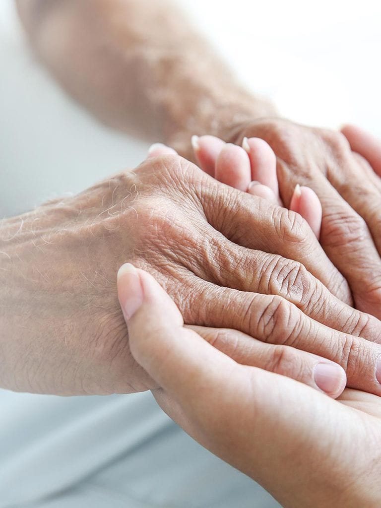 Pflegekraft hält Hände einer pflegebedürftigen Person