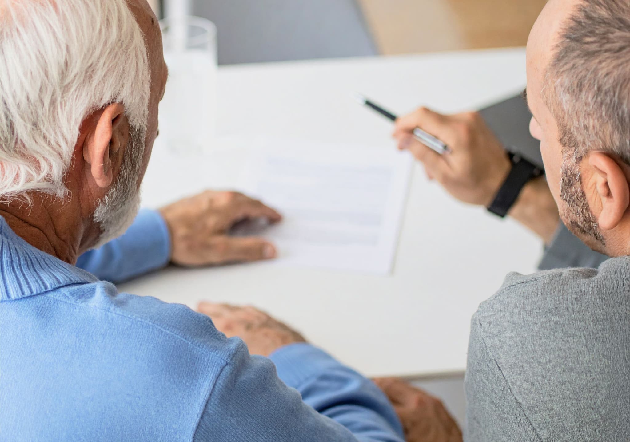 Mann hilft einem älteren Mann, Dokumente am Tisch auszufüllen