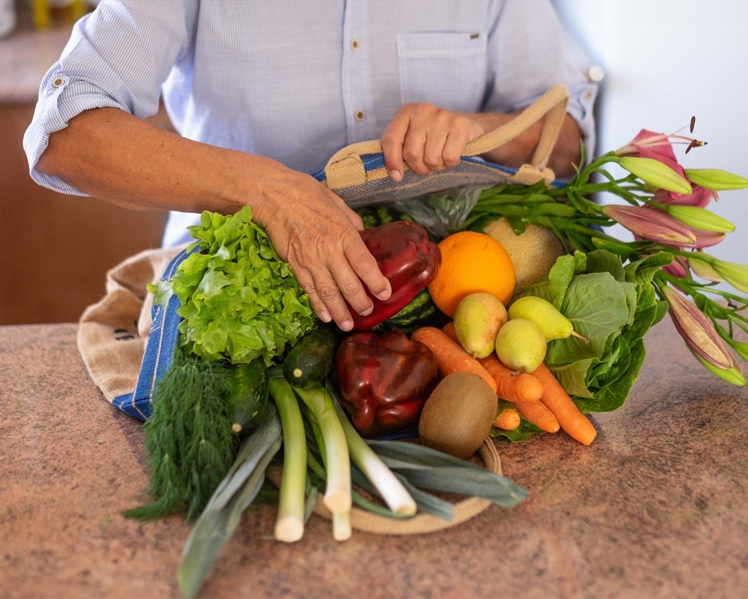 Person legt frisches Gemüse aus einer Einkaufstasche auf eine Küchenarbeitsplatte