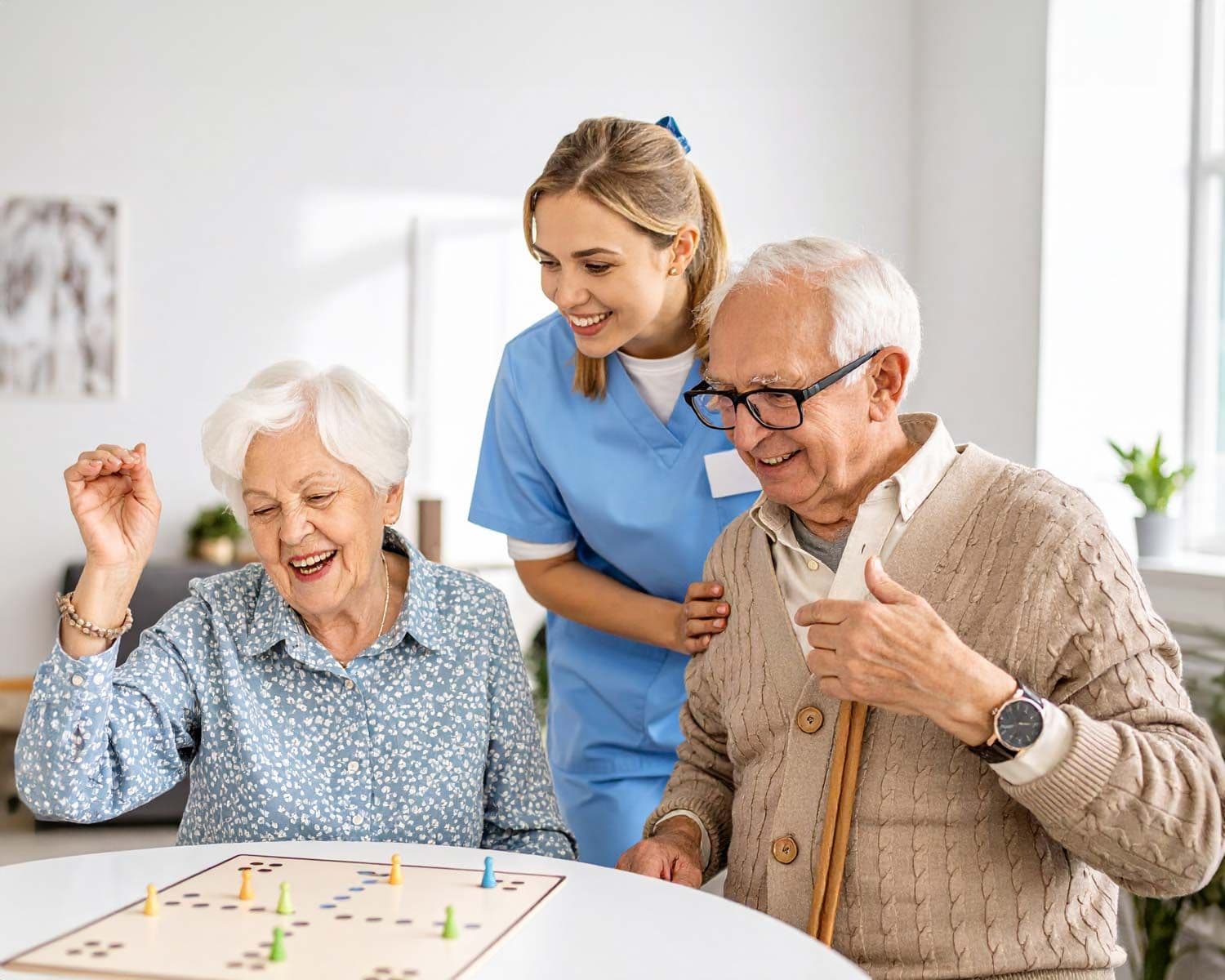 Älteres Paar spielt Brettspiel an einem Tisch, begleitet von einer Pflegekraft
