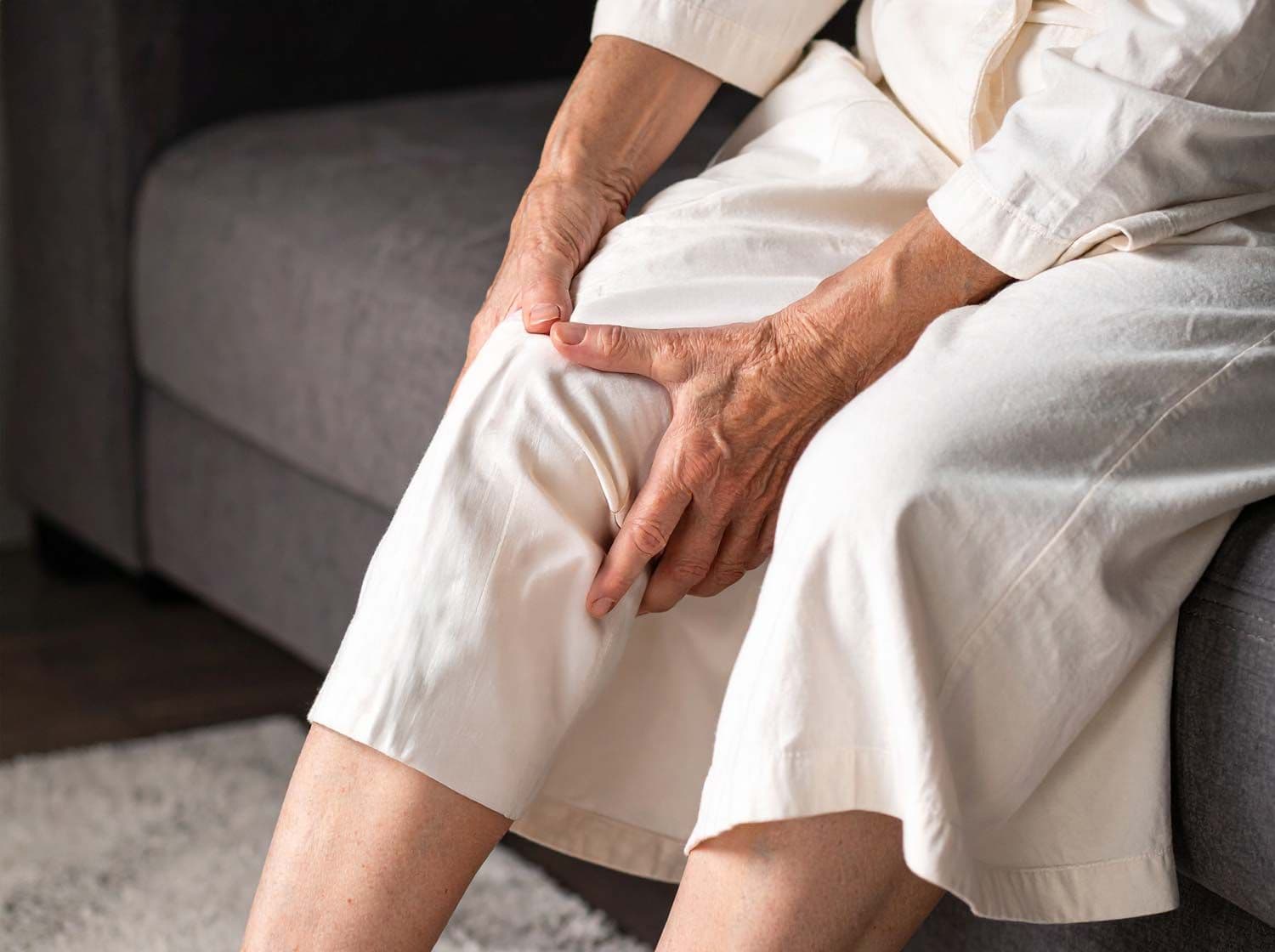 Ältere Frau sitzt auf Sofa und hält schmerzendes Knie