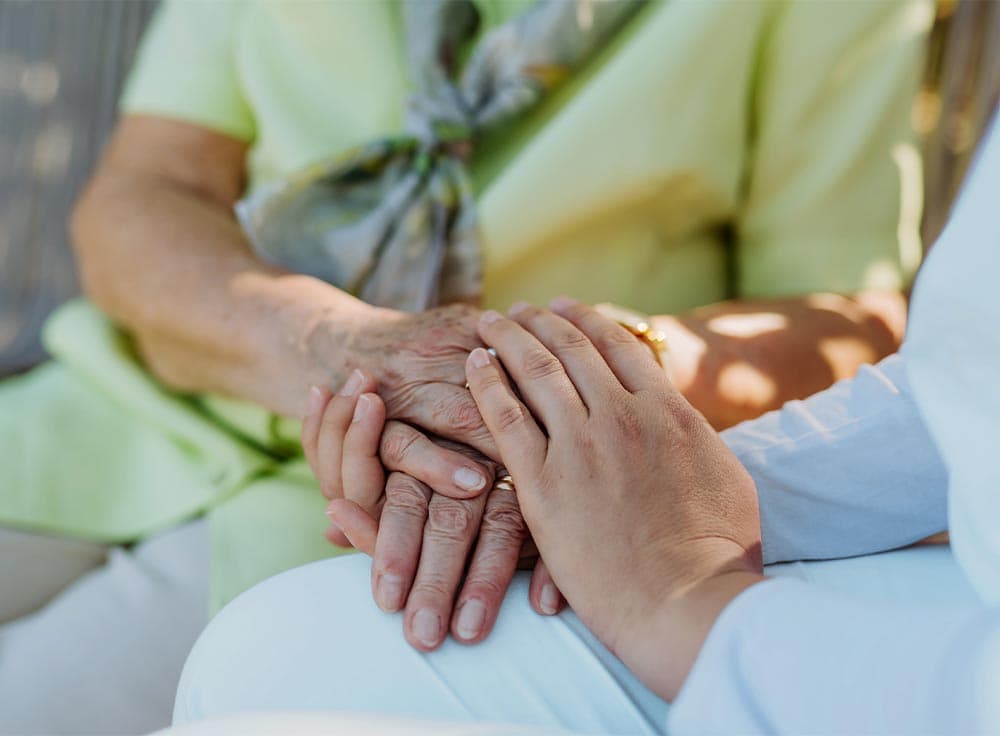 Eine Pflegekraft hält die Hände einer Seniorin – persönliche Beratung zu Pflegehilfsmitteln.