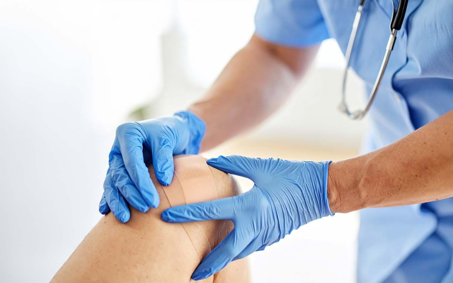 Pflegekraft versorgt Wunde am Knie einer älteren Frau